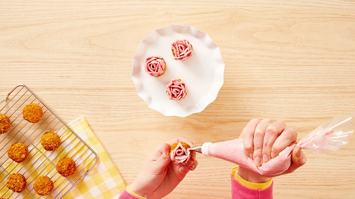 Using a spoon, fill the piping bag and pipe rose shapes onto the cooled pupcakes.