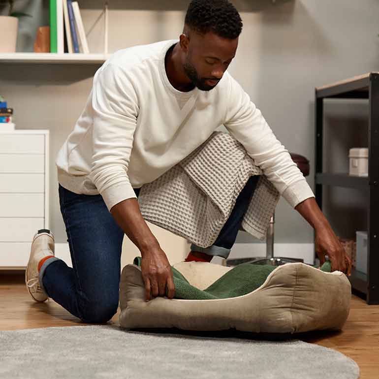 Photo of a man placing a towel into a dog bed