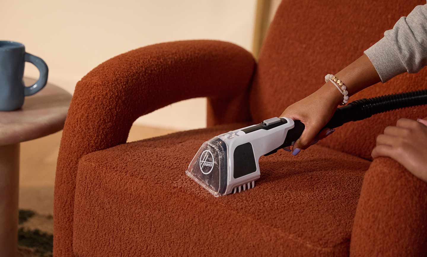 Photo of a woman cleaning an upholstered chair with a handheld vacuum.