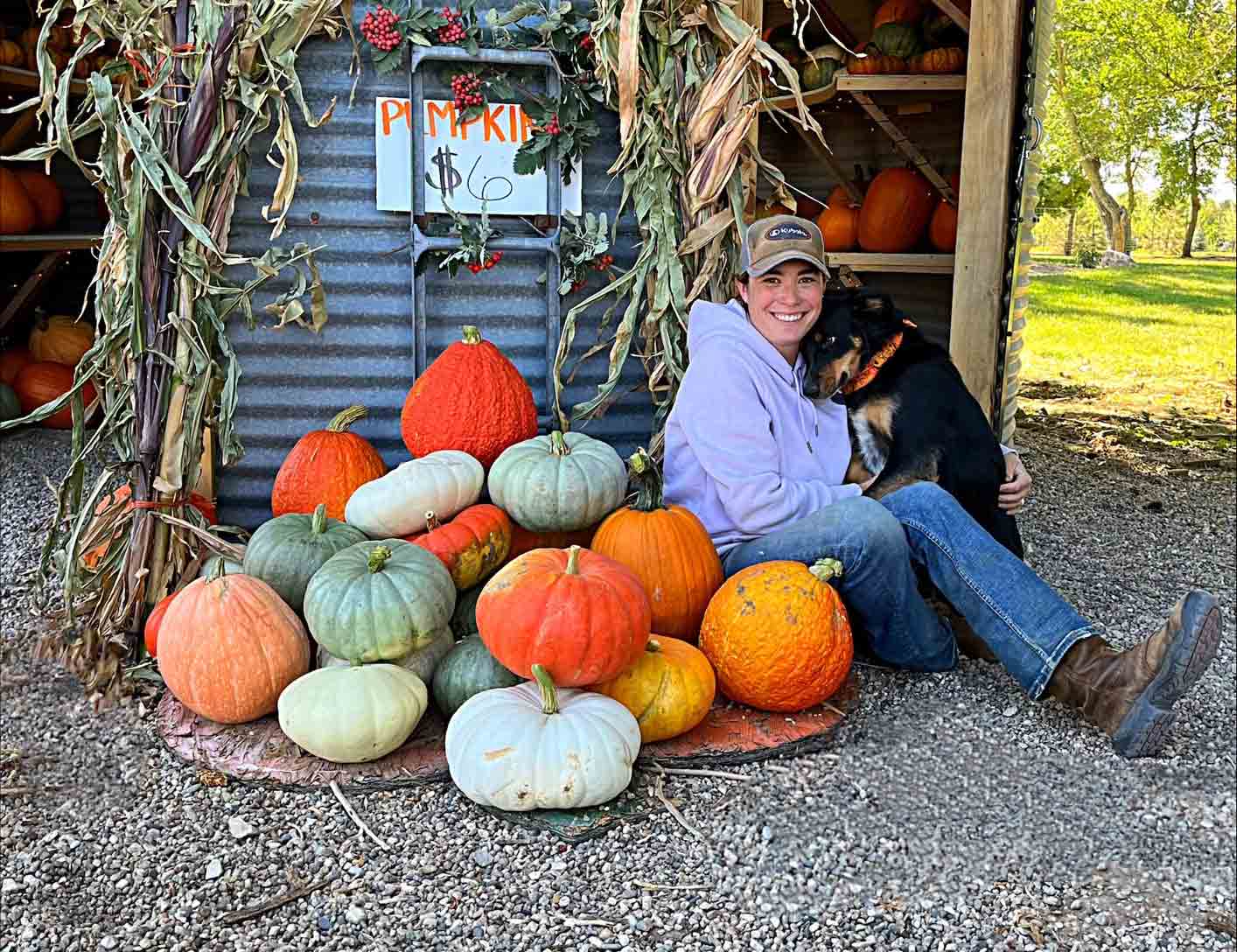 Photo of a woman and dog sitting beside pumpkins at Creekside Valley Farm