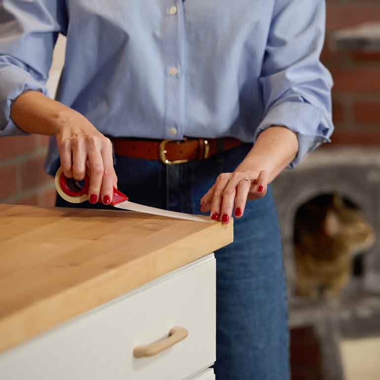 Photo of a woman applying two-sided tape to the top of a kitchen counter