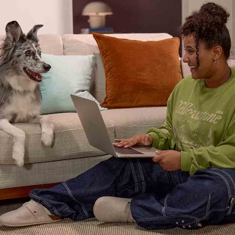 Photo of a woman using a laptop computer beside her dog