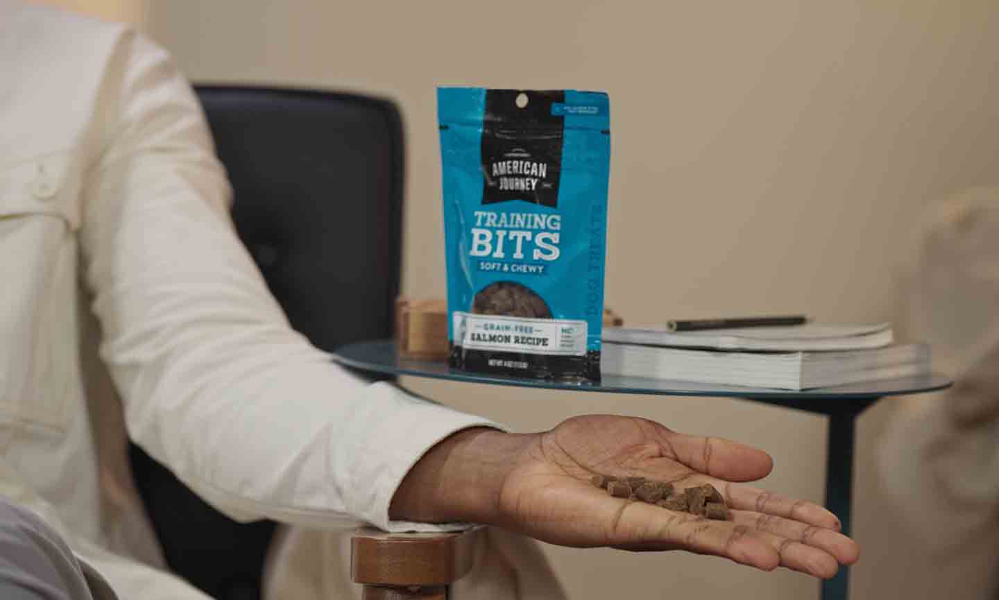 Photo of a man's hand holding dog treats, with the treat bag in the background
