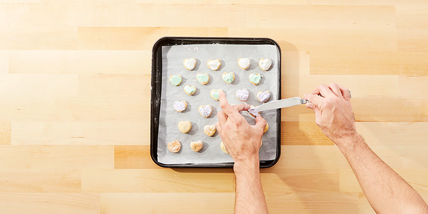 Once the cookies are cooled, use a spoon or butter knife to spread 4 of the frostings evenly across each cookie, setting one frosting aside for decorations.